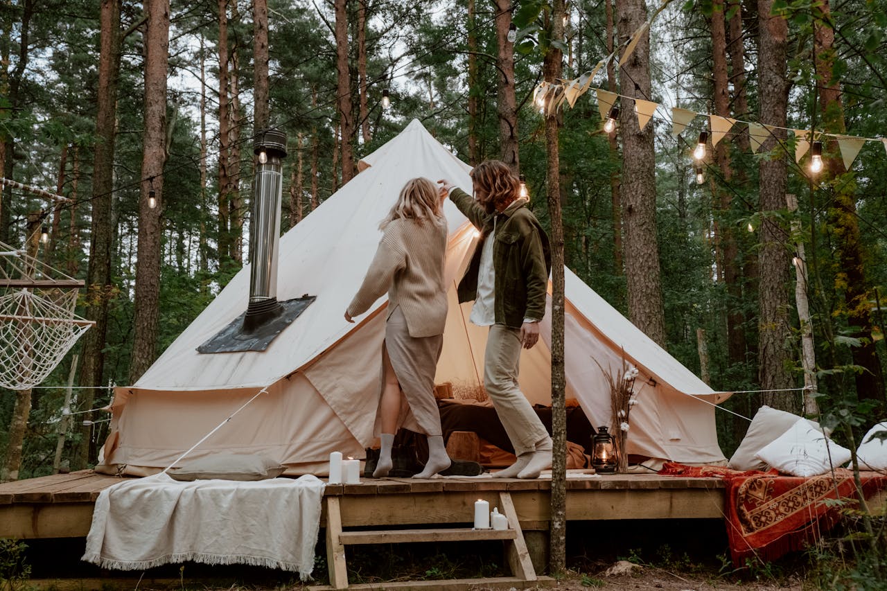 Couple enjoying a romantic evening at a glamping tent in a serene forest setting.